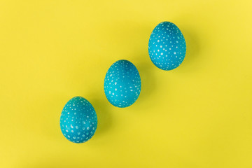 Three blue Easter eggs on bright yellow background, top view