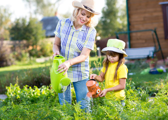 Woman with little girl watering plants in garden