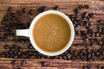 White coffee cup with roasted coffee beans on old wood.