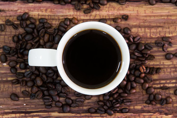 White coffee cup with roasted coffee beans on old wood.