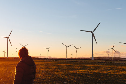 Man Using a Mobile Phone Besides Modern Windmills at Sunset