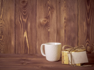 Cup of coffee with gift box on wooden table. Side view