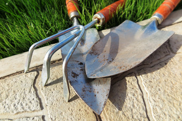 Garden major and minor hand trowels and a flower rake on the tile at lawn in the garden