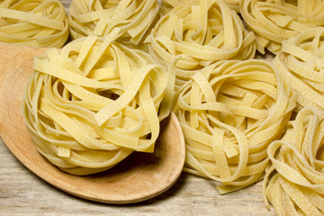 Noodles tagliatelle nests with wooden spoon on wooden background.