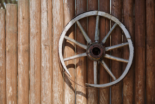 Old vintage wooden carriage cart wheel on the background of wooden logs.
