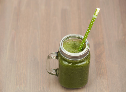 A green smoothie in a mason jar with tube on wooden background