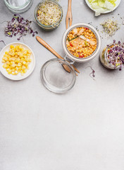 Glass jar salad and vegetables ingredients on light stone background, top view, place for text.  Clean eating, vegetarian or diet food concept.
