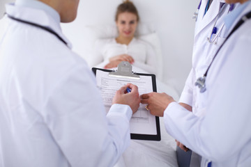 A group of doctors discussing medical history close up , a happy smiling patient in the background.