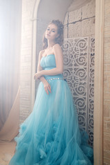 Beautiful young woman in gorgeous blue long dress like Cinderella with perfect make-up and hair style