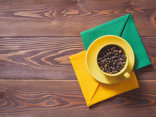 Coffee cup with coffee beans and yellow and green napkins on the wooden table. Top view