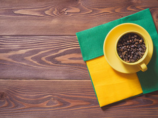 Coffee cup with coffee beans and yellow and green napkins on the wooden table. Top view