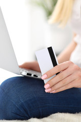 Happy woman doing online shopping at home . Close- up of a hand holding a credit card next to a laptop