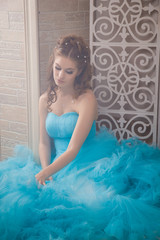 Beautiful young woman in gorgeous blue long dress like Cinderella with perfect make-up and hair style