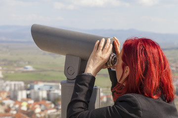 Fototapeta na wymiar Sinj, Croatia, Woman with red hair looking through a coin operated binoculars, rear view