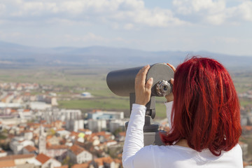 Sinj, Croatia, Woman with red hair looking through a coin operated binoculars,  rear view