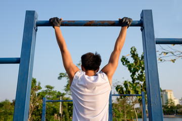 fitness ,sport, exercise, training and lifestyle concept - one young man doing pull ups on horizontal bar outdoors