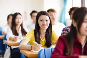 smiling female college student sitting  with classmates