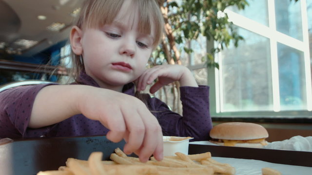 Little girl eating french fries in fast food 