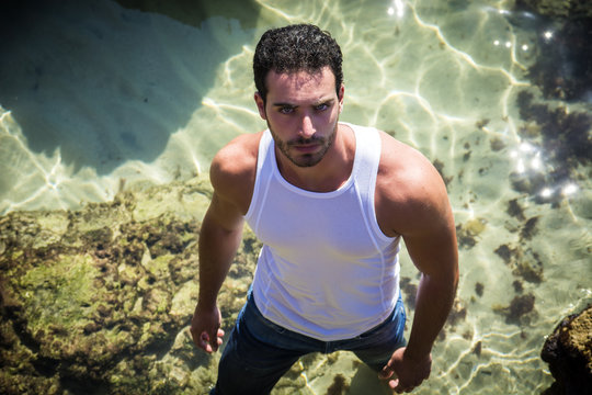 Athletic man in the sea or ocean by rocks, wet t-shirt