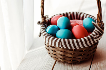 Multicolored Easter eggs in wicker basket on white wooden background