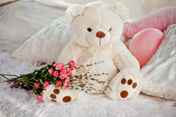 A beautiful soft toy bear sits on the bed with flowers