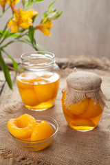 Traditional preserved peaches compote with juice in glass jars on vintage table