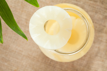 Canned pineapple slices in glass on vintage cloth background top view