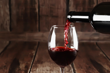 Red wine is pouring from a bottle into a glass - obrazy, fototapety, plakaty