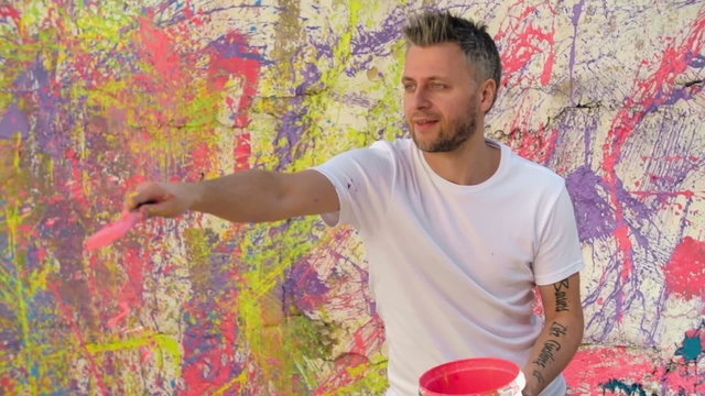 Medium shot of handsome street artist with tattoos on his arms splashing colorful paint on walls in slow motion