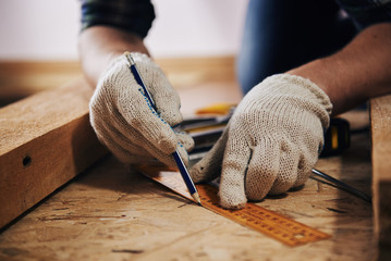 Woodworker with lumber. Professional builder evaluating size of workbench with pencil and ruler.  