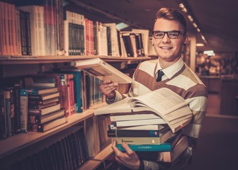 Young attractive librarian holding a pile of books in the university library. - obrazy, fototapety, plakaty