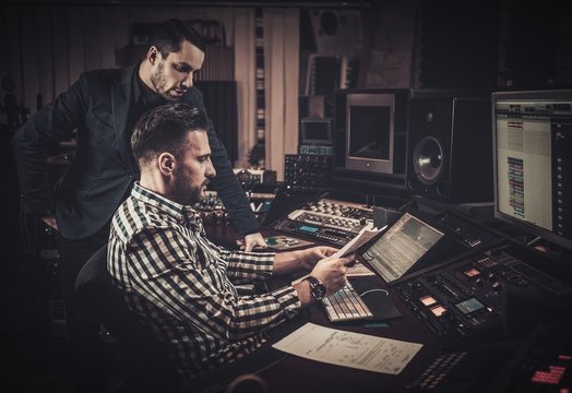 Sound engineer and producer working together at mixing panel in the boutique recording studio.