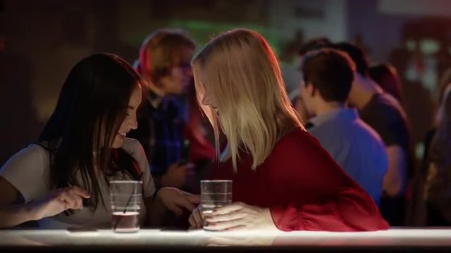 two attractive girls at bar in club talking and laughing