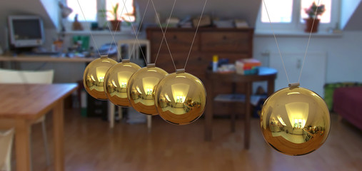 Fünf goldfarbene 3D Pendel mit Tiefenperspektive und Single Wohnung im Hintergrund - Kugelstoßpendel, Newtonpendel, Kugelpendel, Newton-Wiege - Newton's Cradle in Gold.
