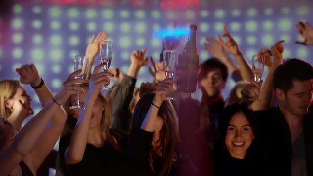 young people on dancefloor at club putting champagne glasses up in the air