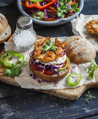 Make fish burger. Ingredients - rye buns, red cabbage, peppers, carrots, herbs and crispy fried fish cutlets on a dark wooden background. Delicious food, rustic style