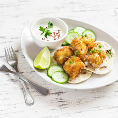 Crispy fried fish on a homemade tortilla on a light wooden background