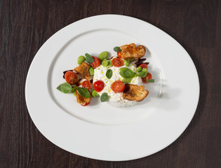 Delicious tomato and mozzarella cheese salad caprese, served on a white plate, with basil, croutons and balsamic vinegar.