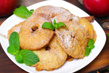 Apples fried in a batter with mint, cinnamon and powdered sugar on wooden table.