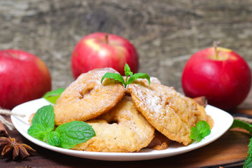 Apples fried in a batter with mint, cinnamon and powdered sugar on wooden table.