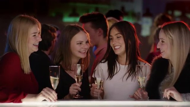 four attractive girls at bar in club with champagne glasses smiling