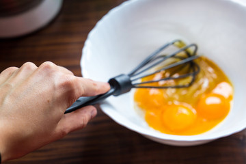 Egg Yolks in a White Big Bowl with Black Beater in Woman Hand, Close-up