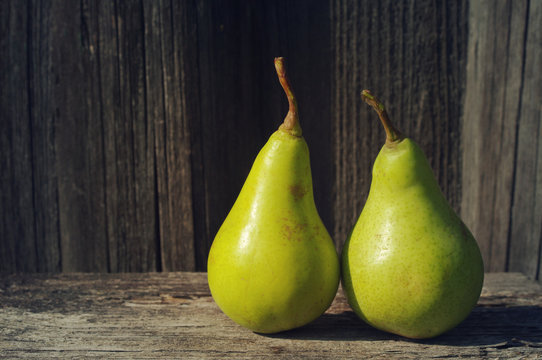 Two fresh green pears against an old textural wooden surface.