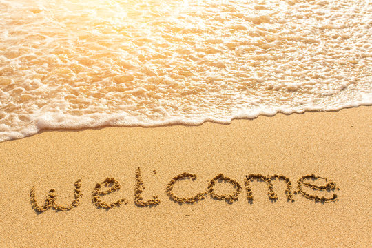 Welcome - drawn on beach sand, soft wave with solar flares.