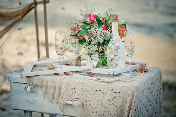 Wedding decor with bottle, glasses, flowers, sea cockleshells and framework for a photo on a ancient suitcase. Decoration of a wedding photoshoot.  Details of a wedding decor in sea style.