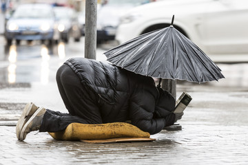 Beggar in the rain with umbrella cars