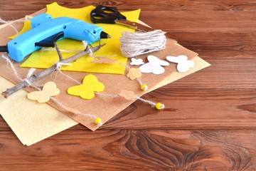 Scissors, hot glue gun, sheets of felt, decorative pendant with felt butterflies and flowers. Wooden background with copy space for text