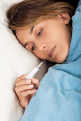 femme au lit malade qui prend sa température