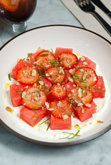 Strawberry and watermelon salad, served with crushed nuts and fresh basil served on a white plate.
