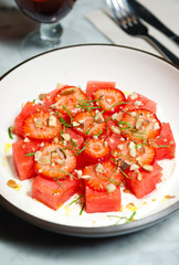 Strawberry and watermelon salad, served with crushed nuts and fresh basil served on a white plate.